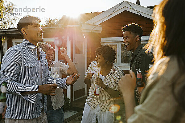 Carefree male and female friends dancing while enjoying drinks in back yard on sunny day at social party