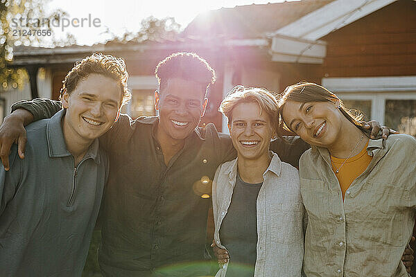 Portrait of happy male and female friends standing side by side in back yard at social party