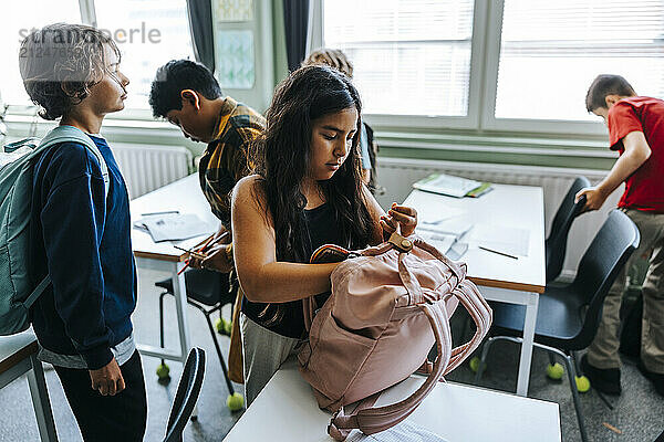 Schoolgirl packing bag while standing in classroom