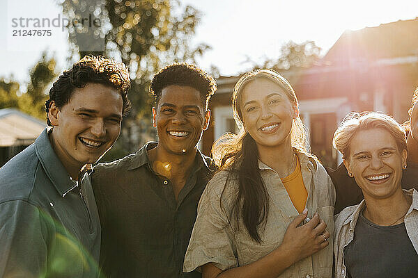 Portrait of happy male and female friends in back yard on sunny day at social party