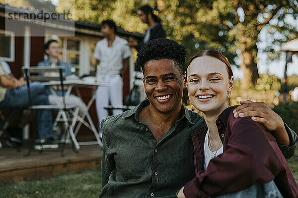 Portrait of happy young man with arm around female friend in back yard