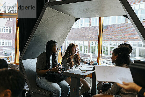 Female students studying while sitting in hexagon structure at school