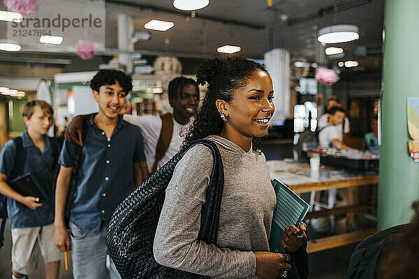 Smiling teenage girl with bag walking in cafeteria at junior high school