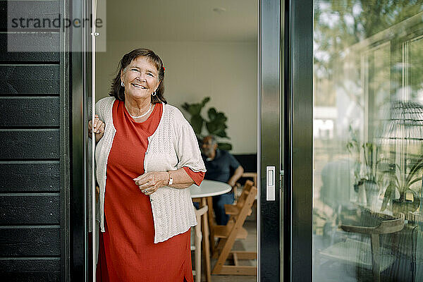 Portrait of smiling senior woman leaning on house doorway