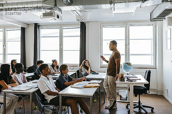 Male teacher teaching group of junior high students sitting in classroom at school