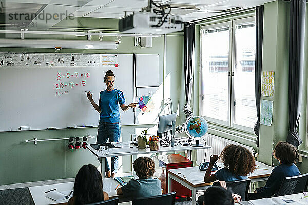 High angle view of female professor teaching mathematics to group of multiracial students in classroom at school