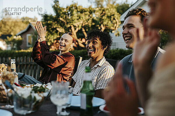 Happy male and female friends sitting together at dining table in back yard