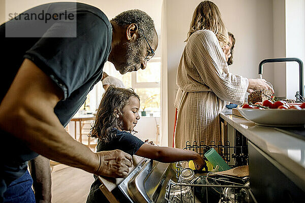 Grandfather assisting grandson loading utensils in dishwasher at home