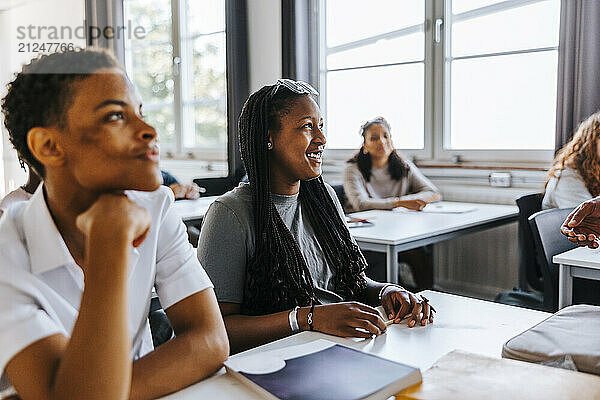 Happy teenage girl sitting beside male classmate near desk in classroom at junior high school