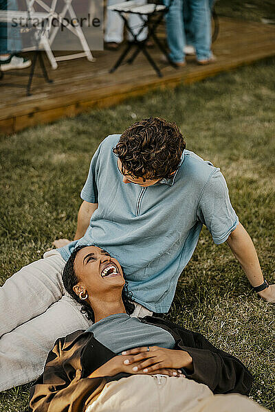 High angle view of happy woman lying down on lap of male friend sitting on grass in back yard