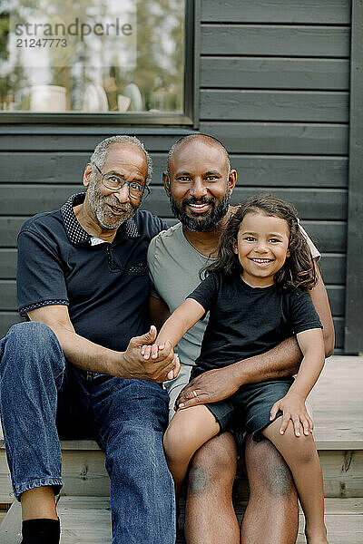 Portrait of senior man sitting with son and grandson on porch