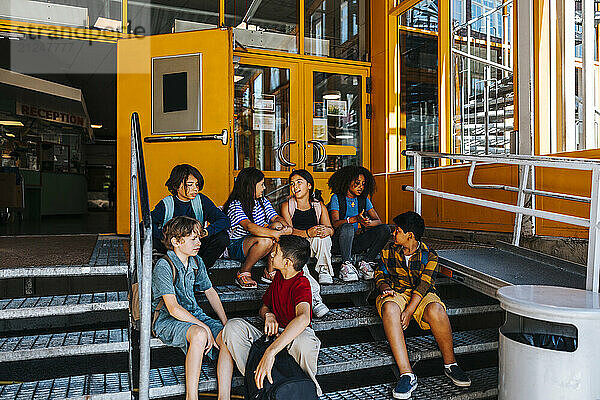 Male and female friends sitting on stairs in front of school building