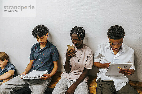 Male multiracial students spending leisure time sitting on bench near wall at school