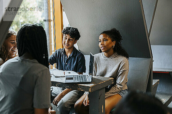 Group of multiracial students studying through laptop in cafeteria at junior high school