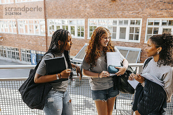 High angle view of multiracial female students discussing with each other while standing near railing in balcony at scho