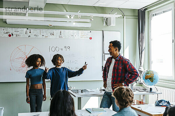 Professor with students explaining mathematics equations to pupils in classroom at school