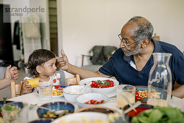 Grandfather talking to granddaughter sitting at dining table during lunch at home