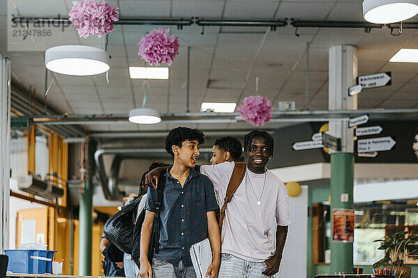 Smiling teenage boy walking with arm around male friend in cafeteria at junior high school