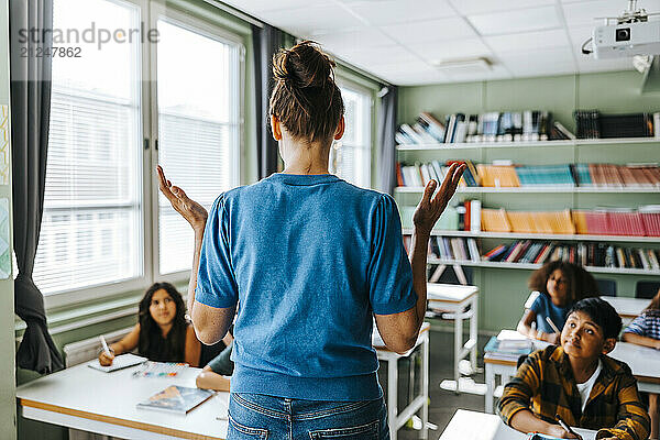 Rear view of female teacher with hair bun teaching group of elementary students in classroom at school