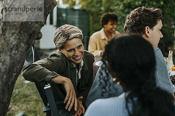 Happy blond hair woman talking with female friend while sitting in back yard for dinner party