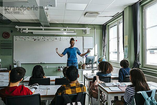 Female professor with arms outstretched teaching group of students in classroom at elementary school