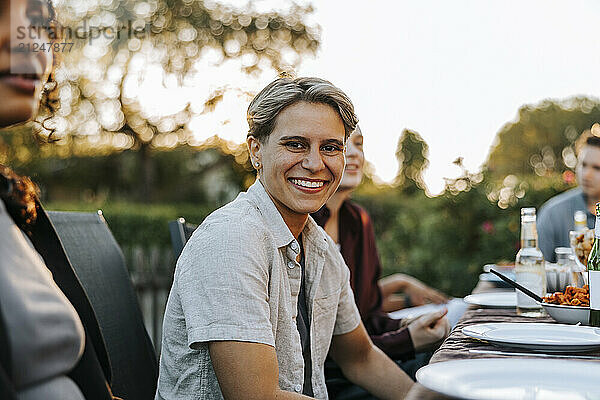 Portrait of smiling young woman with short hair sitting near table in back yard at social party