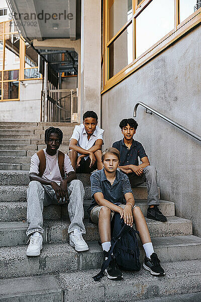 Portrait of multiracial teenage boys sitting on stairs of school building