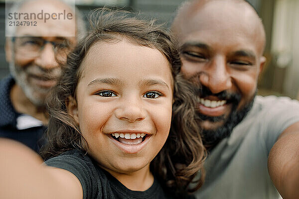 Close-up portrait of smiling boy taking selfie with father and grandfather