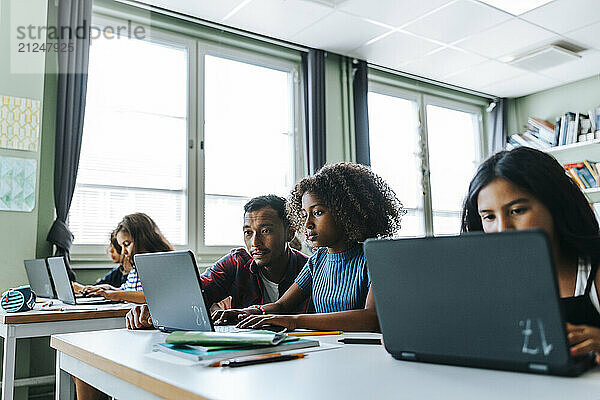 Male teacher assisting girl studying on laptop in classroom at elementary school