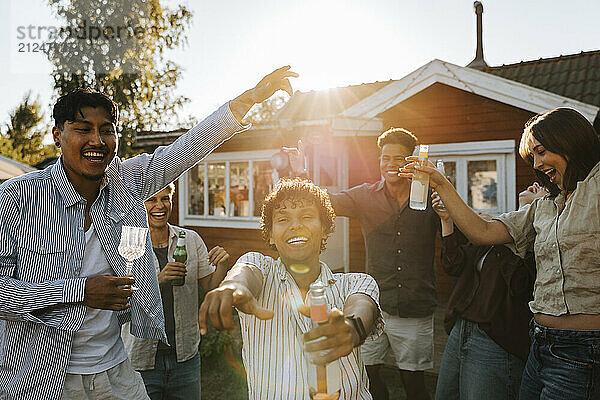 Carefree multiracial group of male and female friends enjoying drinks while dancing in back yard at party