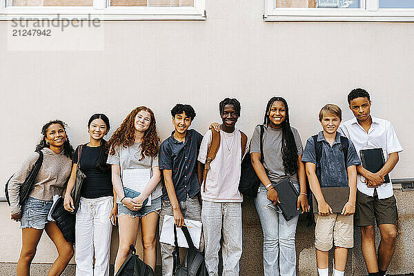 Portrait of multiracial male and female junior high students standing side by side near wall of school building