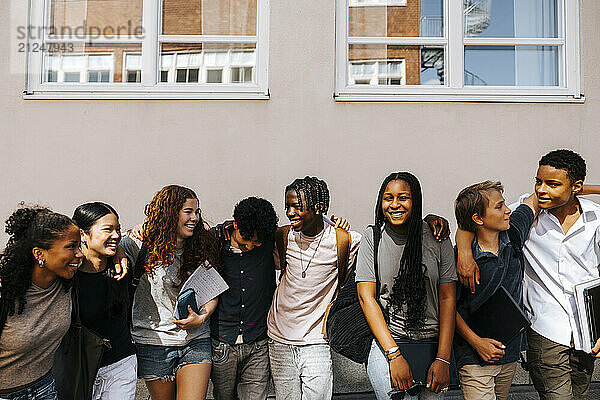 Multiracial male and female junior high students standing side by side near wall of school building