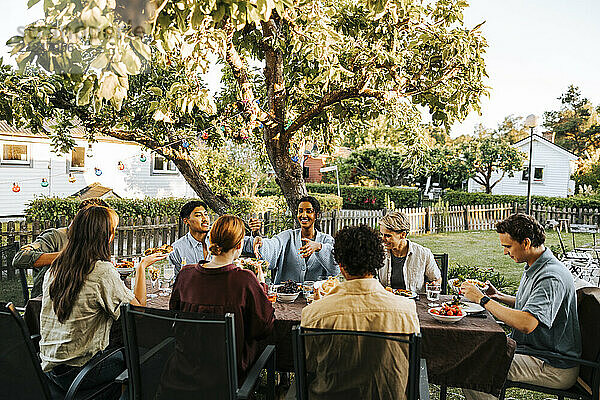 Male and female friends having dinner in back yard at social gathering