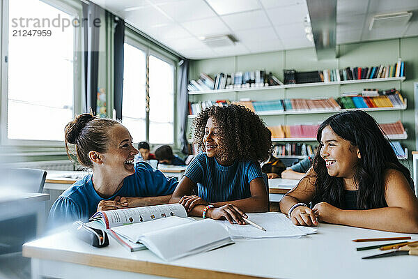 Happy female teacher crouching near schoolgirls sitting near desk in classroom