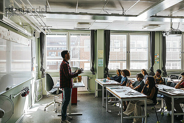 Side view of male professor teaching group of students in classroom at elementary school