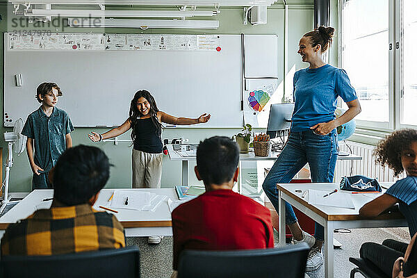 Happy girl standing with arms outstretched in front of whiteboard in classroom at school