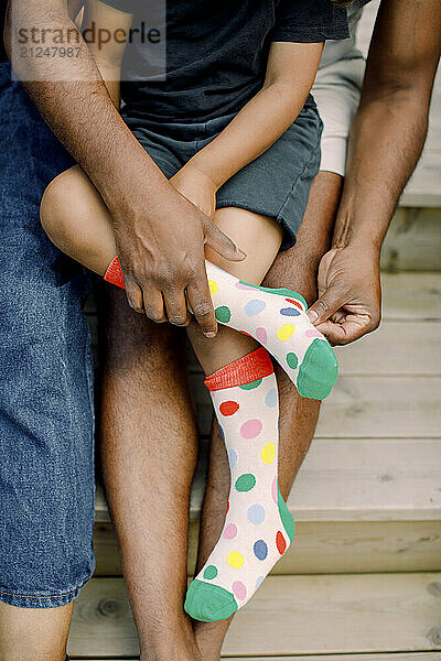 Hands of father helping son while wearing colorful socks