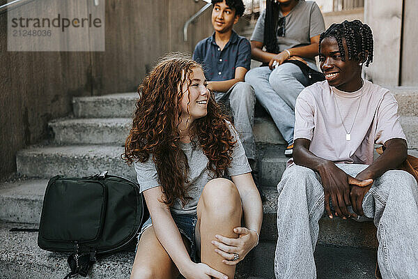 Happy teenage girl sitting with friends on stairs of junior high school