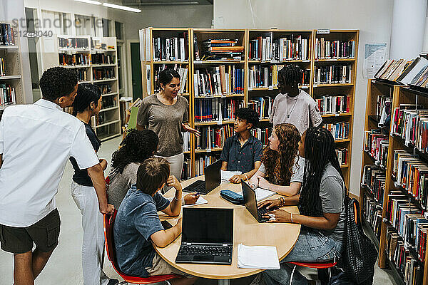 High angle view of female professor teaching group of male and female students in library at junior high school