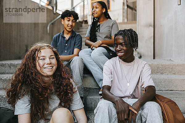 Happy teenage boy sitting with friends on stairs of junior high school