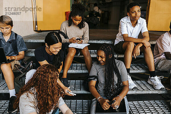 High angle view of male and female junior high students spending leisure time while sitting on steps in front of school