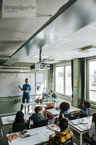 High angle view of female professor teaching mathematics to group of elementary students in classroom at school