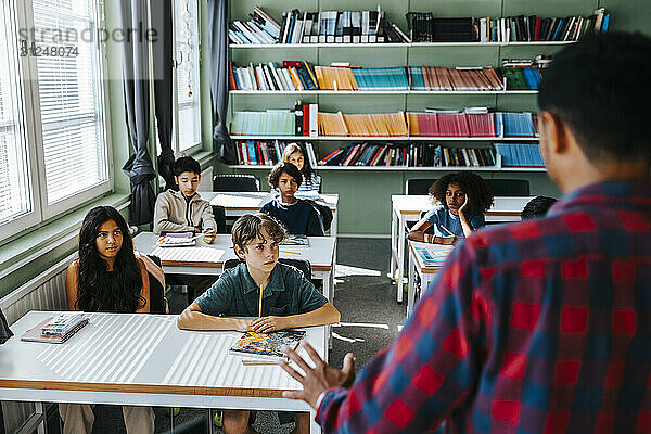 High angle view of group of students sitting near desk while male teacher teaching in classroom at school