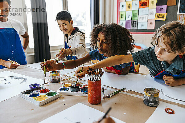 Male and female students painting in art class at elementary school