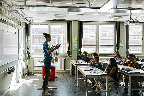 Side view of female professor teaching group of students in classroom at elementary school