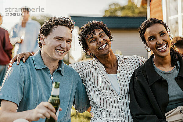 Cheerful young man with arm around friends in back yard at dinner party