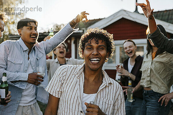 Portrait of happy curly hair man dancing with friends in back yard at social gathering