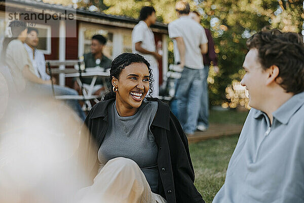 Happy young woman talking with male friend while sitting in back yard