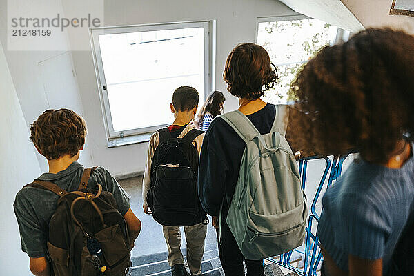 Rear view of male and female students moving down stairs of school building