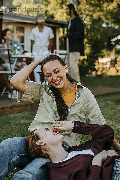 Happy woman lying down on lap of female friend sitting on grass in back yard